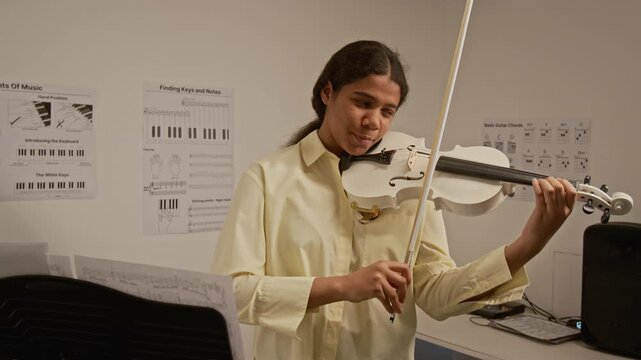 Black female teenager playing violin in music classroom, looking at camera and smiling. Footage for music school advertisements and arts education campaigns