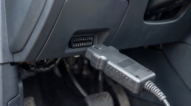 Hand connecting obd ii diagnostic scanner to car, auto repair and maintenance, vehicle diagnostics, automotive technology, checking engine light code, service station equipment.