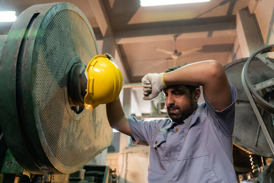 Exhausted technician wiping sweat and showing fatigue while repairing heavy machinery in industrial factory.