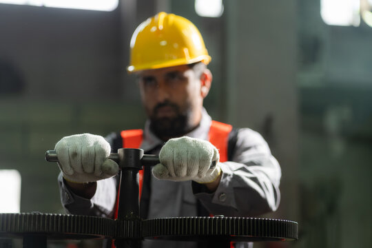 Close-up of technician wearing gloves and hardhat turning valve to operate heavy machinery in industrial factory.