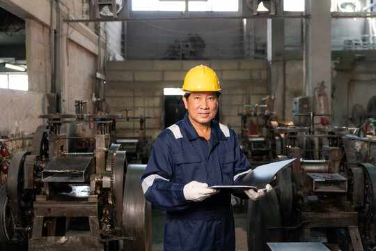 Portrait of confident senior engineer smiling while holding folder report in industrial factory.