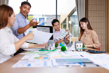 Fototapeta premium Group of business people discussing charts and house models during a meeting in a bright office, with presentation papers and a teamwork atmosphere