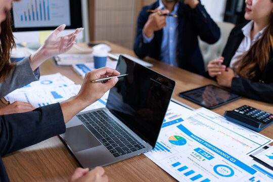 Business people discussing sales charts and financial reports around a laptop in a modern office meeting.