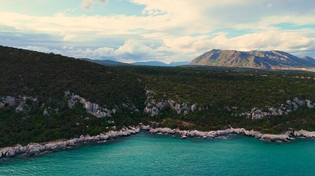 Aerial View of Serene Coastal Landscape with Turquoise Water and Lush Green Hills under a Cloudy Sky. Sardinia holiday trip.