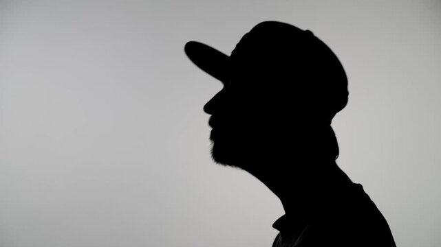 A close-up of an anonymous silhouette of a man making strange neck movements against a white wall