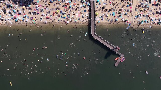 Aerial drone view of a crowded summer lake beach with people swimming and sunbathing. Colorful umbrellas, water obstacle course on lake, on a sunny day. Lake Pogoria in Dabrowa Gornicza, Poland