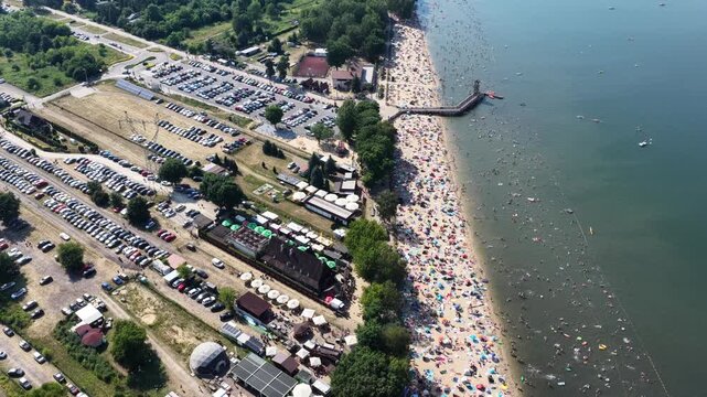 Aerial drone view of a crowded summer lake beach with people swimming and sunbathing. Colorful umbrellas, water obstacle course on lake, on a sunny day. Lake Pogoria in Dabrowa Gornicza, Poland