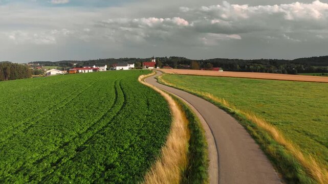 Flying low over a scenic narrow road winding through fields towards a village in a rural area