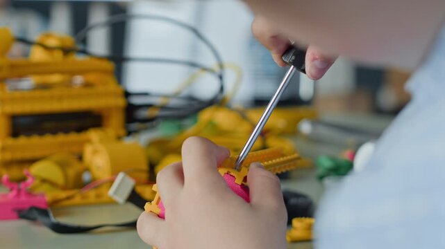 Child using screwdriver to assemble plastic robot parts during robotics lesson. Footage is ideal for promoting STEM education, modern school curriculums, and children science camps