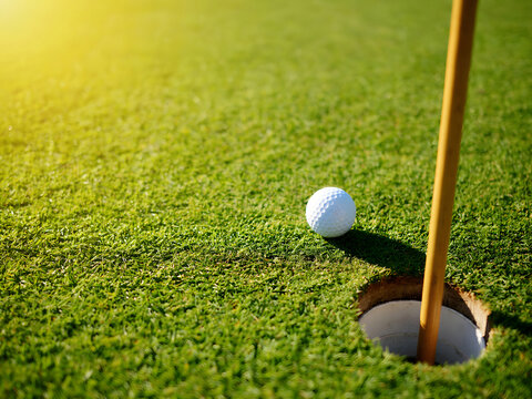Golf ball near hole with flagstick on green grass course, sunny day