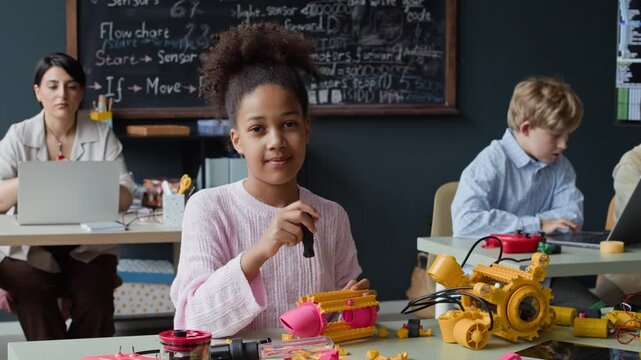 Portrait of African American female child assembling robot toy with screwdriver in STEM class and smiling. Video is perfect for marketing elementary school science and technology programs