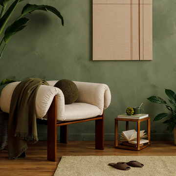 Cozy living room interior with stylish beige armchair, green wall, tropical plants, and modern home decor