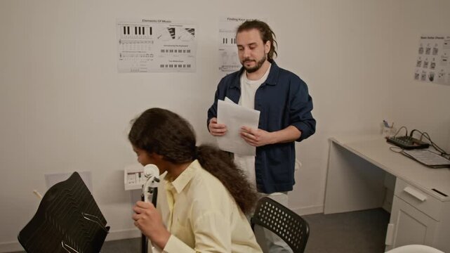 Zoom out shot of Caucasian music teacher explaining sheet music to African American teenager holding violin. Ideal for promoting private music lessons, arts education, and creative tutoring