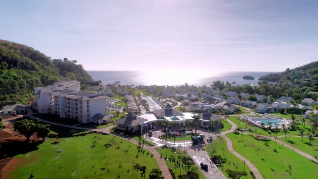 High-angle aerial drone shot capturing a comprehensive view of a luxury Caribbean resort, showcasing villa architecture, extensive landscaped gardens, swimming pools, and the scenic ocean horizon