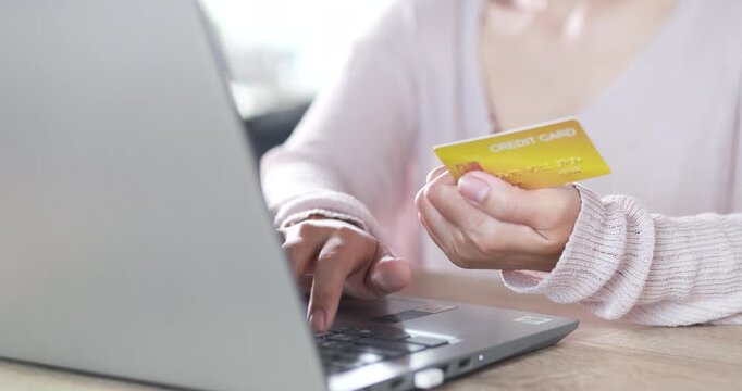 Close-up of a woman holding a credit card while using a laptop for online payment. e-commerce, secure digital transaction, online shopping, fintech, and cashless payment