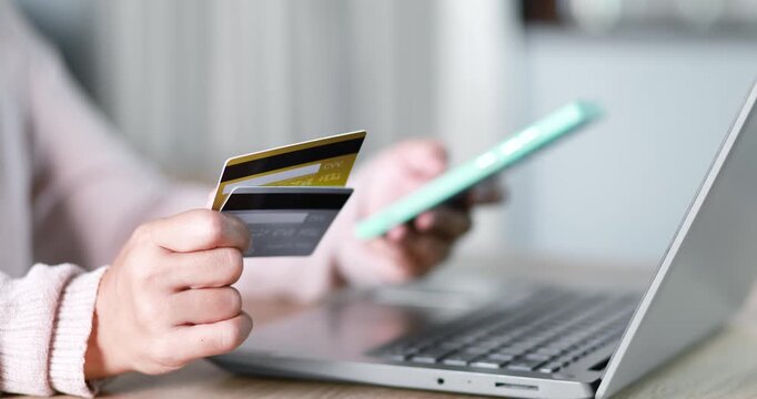 Close-up of a woman holding a credit card while using a laptop for online payment. e-commerce, secure digital transaction, online shopping, fintech, and cashless payment