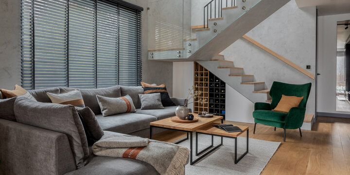 Modern open-plan living room interior with stylish grey sofa, wooden coffee tables, and contemporary staircase design