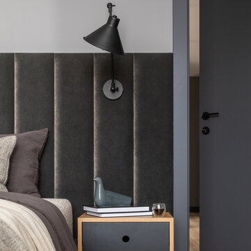 Modern Bedroom Interior with Dark Headboard, Bedside Table, Wall Lamp, and Decorative Elements