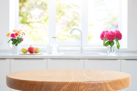 Round wooden  table with blurred background of a bright modern kitchen with flowers and fruits.
