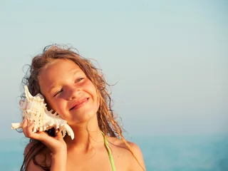 Happy child girl listening to seashell at beach. Young girl holding conch shell to her ear to hear ocean sound. Summer vacation activity, childhood holiday, leisure travel concept. © Tatyana Gladskih