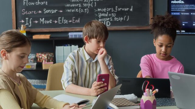 Diverse children using laptops and smartphone during robotics lesson in classroom. Clip is perfect for marketing STEM education, coding bootcamps, and modern school programs