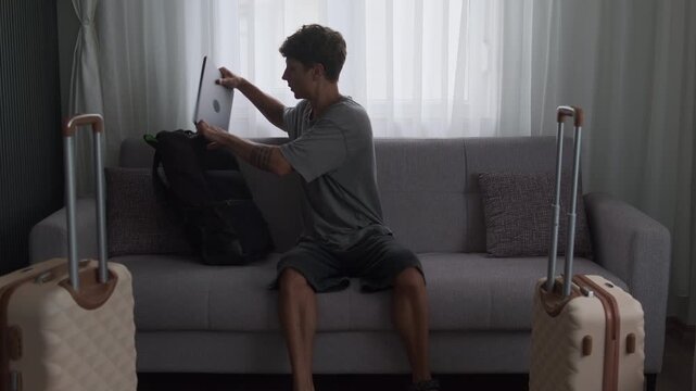 Digital nomad rush and relocation stress. Freelancer finishing remote work, packing laptop into backpack and leaving apartment with luggage
