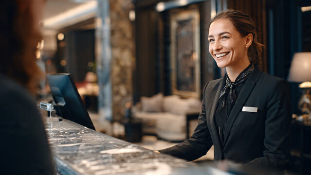 Professional receptionist welcoming and assisting a client at the front desk of a modern hotel lobby, business hospitality concept highlighting excellent customer service, check-in assistance.