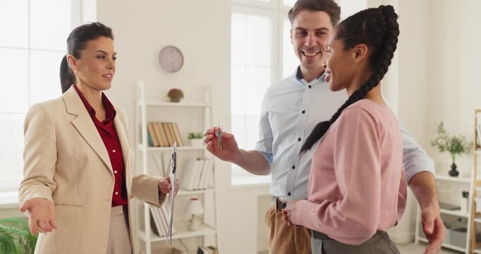 Couple consults realtor and agent about keys. They discuss property options, contract details, rental or buy choice in an apartment while planning move in. Clear concept of guided home choice.