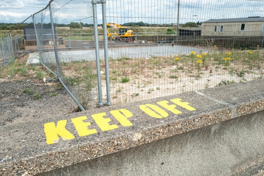 Shallow focus of a stencilled Keep Off sign on a flood and tide wall located in Hunstanton, Norfolk, UK. In the background a new beachside house will soon be built.