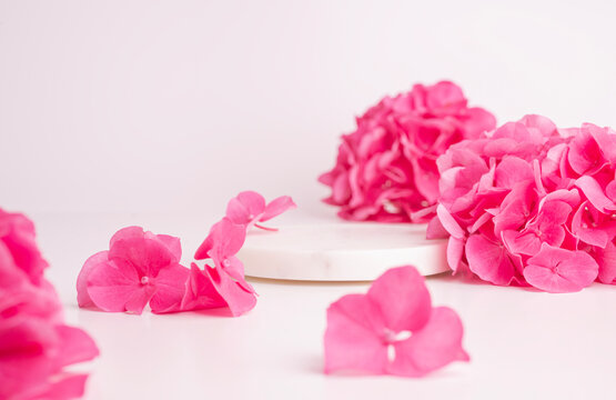 Мarble product display podium with pink hydrangea flowers on a light background.