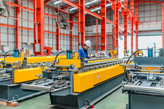 Young female engineer inspecting metal sheet roll forming production line with tablet in factory