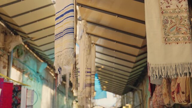 Traditional jewish prayer shawls, known as tallit, hanging in a historic market alley in Jerusalem's Old City, gently moving in a sunlit breeze, a symbol of faith and heritage