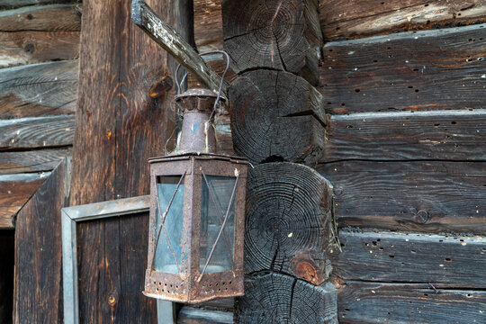 Antique square metal lantern with glass panes and heavy rust patina hanging from wooden peg