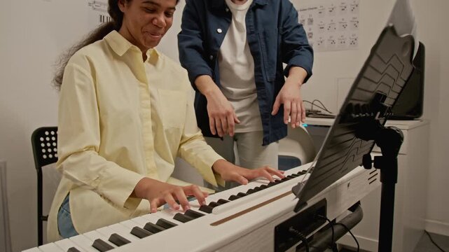 African American girl practicing digital piano while Caucasian male instructor guiding her hand posture. Clip for music school promos and tutoring advertisements