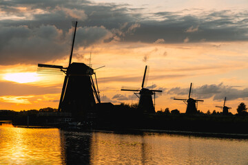 Kinderdijk windmills silhouetted at sunset, golden sky reflecting in canal water, Netherlands historic landscape © Víctor Sánchez