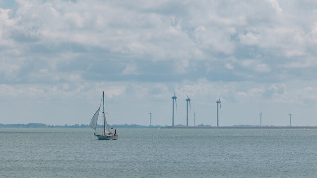 Sailboat navigating past a wind farm in the Zeeland waters, symbolizing sustainability and renewable energy