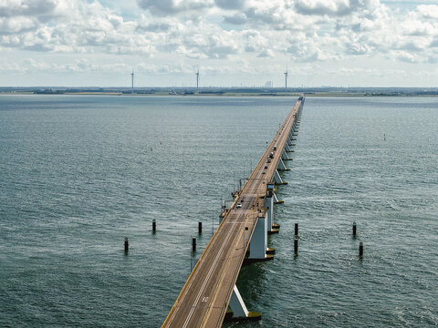 Zeeland Bridge spanning Oosterschelde estuary, long concrete structure with traffic, distant wind turbines on horizon