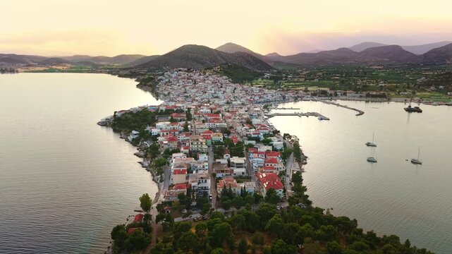 Aerial sunset panorama of Mediterranean town of Ermioni featuring red rooftops, marina, mountain backdrop and golden hour Greek coastline