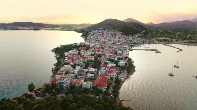 Aerial approach toward Ermioni, Greece, at sunset showcasing the picturesque coastal town surrounded by the Aegean Sea