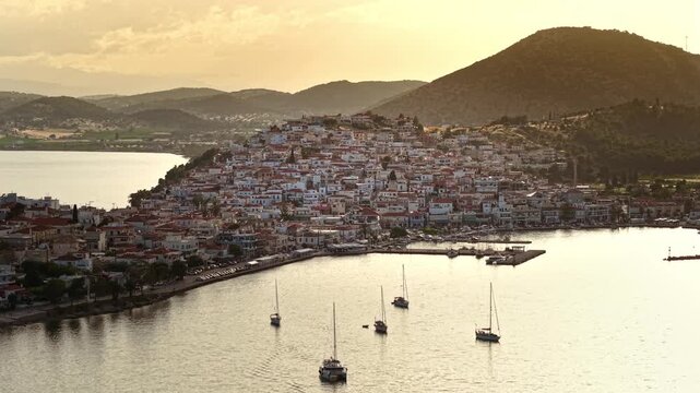 Wide Aerial view of Ermioni Harbor with Anchored Sailboats on calm Aegean Sea reflecting a warm Golden Sunset. Peloponnese, Greece