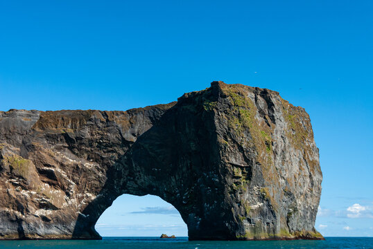 Dyrh&oacute;laey sea arch in South Iceland with dramatic basalt cliffs rugged Atlantic coastline and spectacular volcanic rock formations beneath a clear blue sky