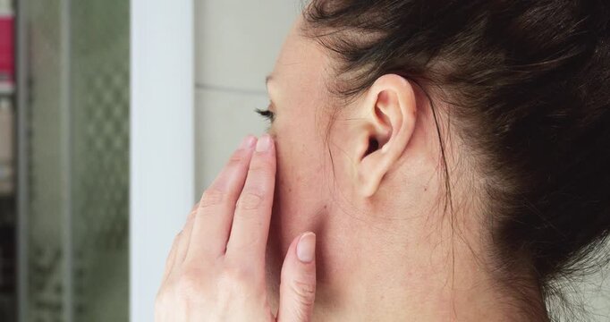 Young woman examines skin texture in bathroom mirror. Skincare routine highlights beauty care and self-confidence. Natural light enhances atmosphere of self-care.