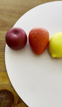 Top view of premium illusory glazed mousse desserts shaped like realistic fruits on a white circle display over a wooden background.