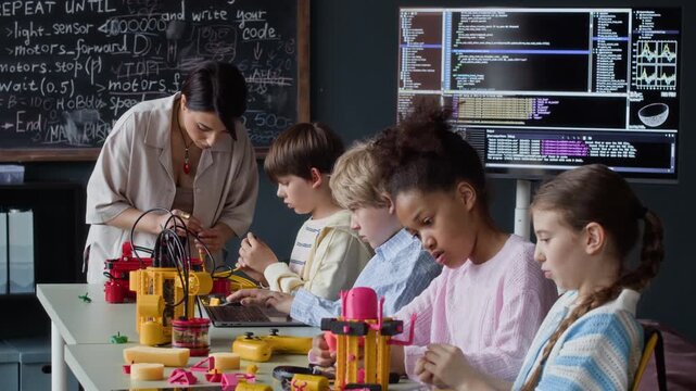 Multiethnic children building robotic models in classroom with female teacher helping them. Video is perfect for promoting STEM education, school programs, and modern learning technologies