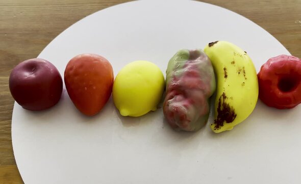 Top view of premium illusory glazed mousse desserts shaped like realistic fruits on a white circle display over a wooden background.