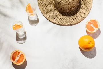 A straw hat and fresh grapefruit slices with cold glasses of water on a sunny surface under palm leaf shadows, tropical vacation vibe, refreshing lifestyle, summertime drinks. © magic_cinema