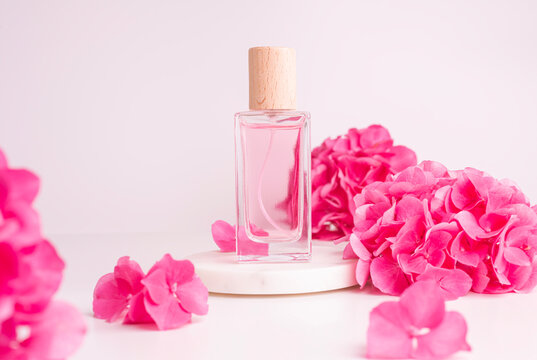 Pink floral perfume bottle display on white pedestal with blooming hydrangea petals