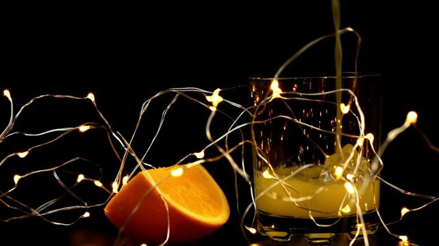 Orange juice is poured into a glass, an orange slice is nearby, a garland