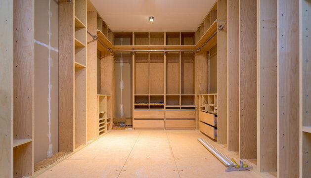 Empty Custom Built Plywood Walk-in Closet with Extensive Shelving and Drawer System in a Modern Home Under Construction