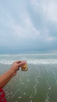Seashells on the bottle on the seabeach. Selective focus of a small bottle in hand with tiny shells on beach sand. keep moment in little bottle. Collecting pebbles on a glass bottle. 